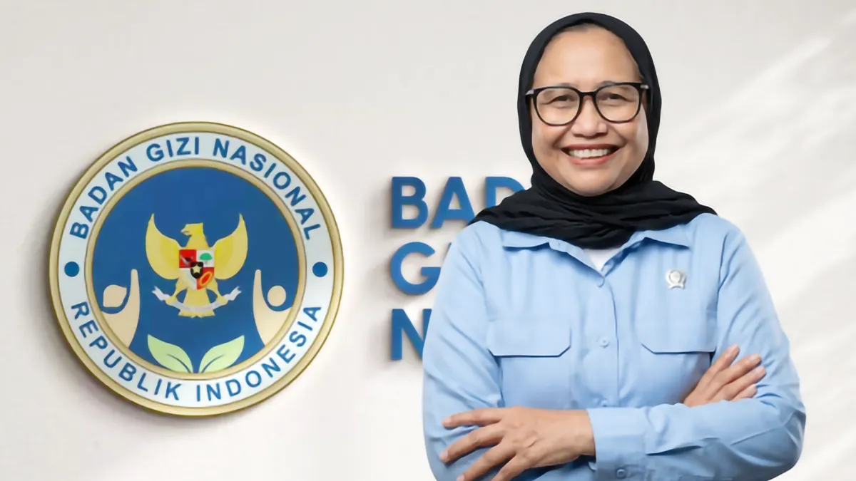Kepala Badan Gizi Nasional Nanik Sudaryati Deyang tersenyum bersedekap di depan logo BGN