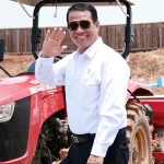 Menteri Pertanian Andi Amran Sulaiman tersenyum melambaikan tangan di depan traktor merah di area lahan pertanian