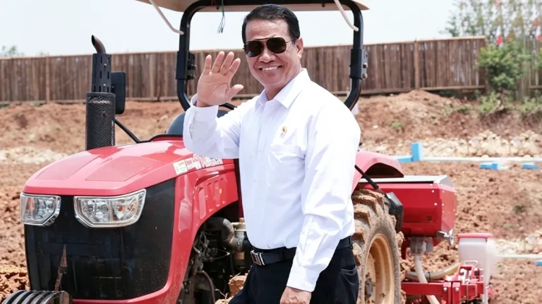 Menteri Pertanian Andi Amran Sulaiman tersenyum melambaikan tangan di depan traktor merah di area lahan pertanian